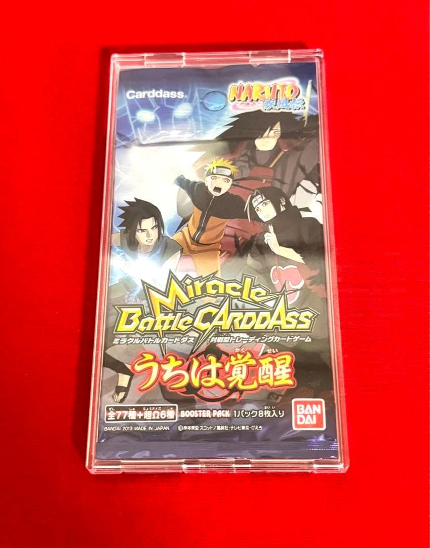 Front of an unopened Miracle Battle Carddass NARUTO booster pack in a clear protective case on a red background.