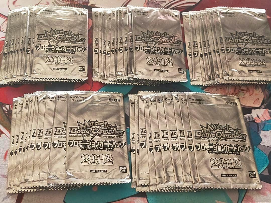 Many sealed silver Miracle Battle Carddass promotion card packs labeled “2012” and “NOT FOR SALE” arranged on a surface.