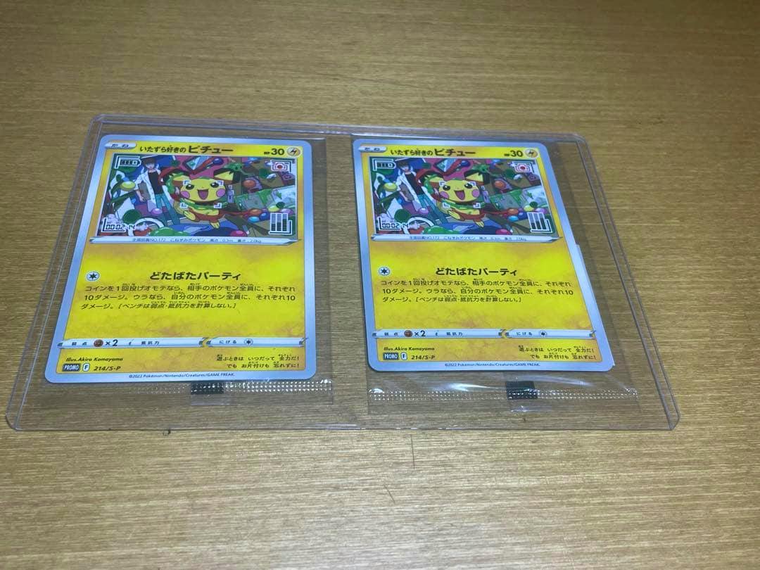 Two いたずら好きのピチュー Pokémon trading cards in clear plastic sleeves on a wooden surface.