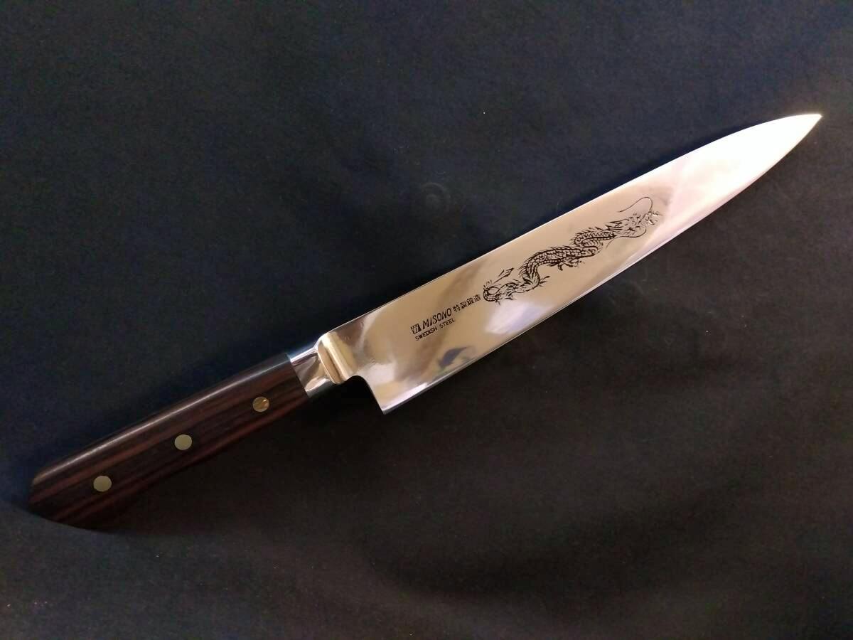 Full Misono chef knife with a wooden handle and dragon engraving on the blade lying on a dark background.