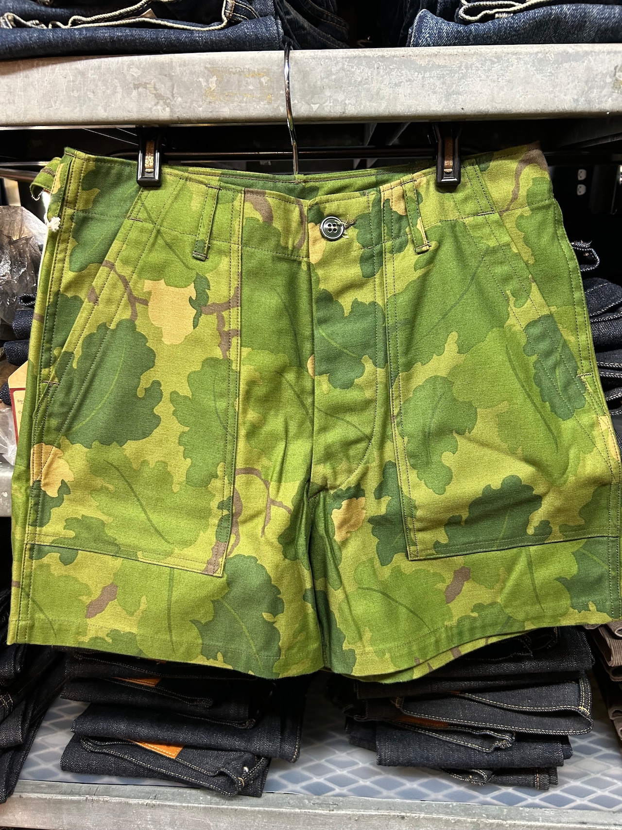 Front view of men's Mitchell-pattern camouflage cotton shorts hanging on a clip hanger.