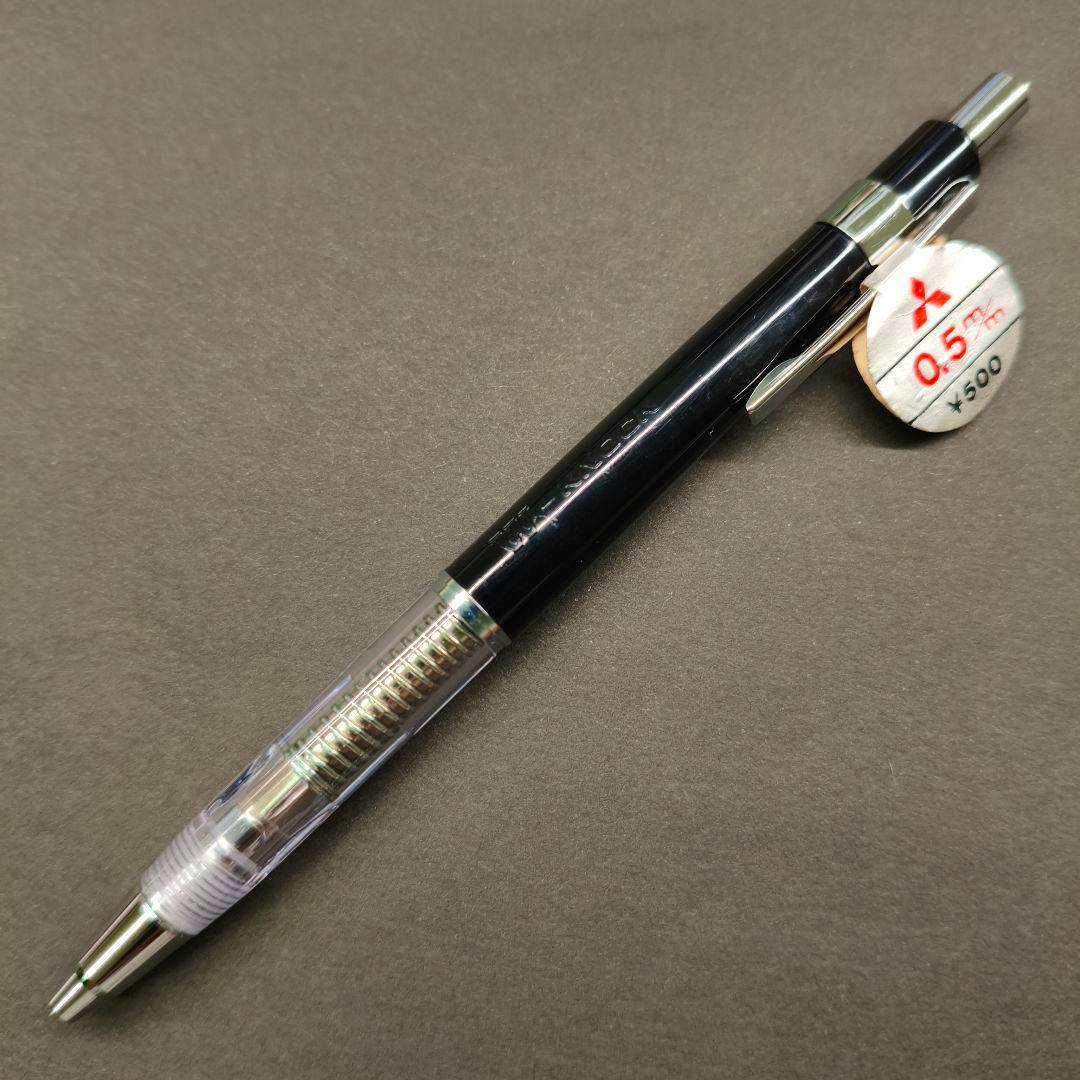A Mitsubishi transparent double-knock mechanical pencil (0.5 mm) with a black barrel photographed on a dark background.