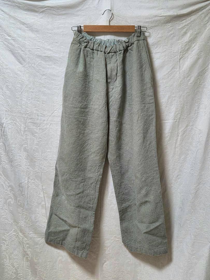 Wide linen pants (MITTAN, size 2) hanging on a wooden hanger against a white textured backdrop.