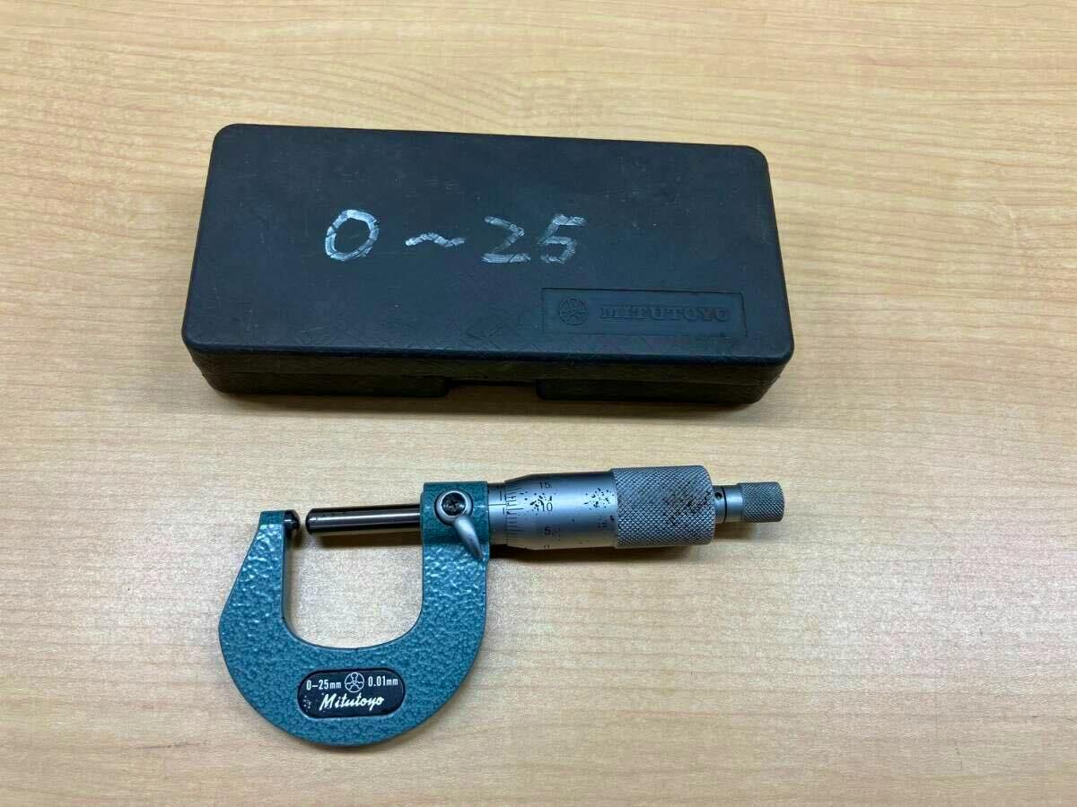 Mitutoyo 0–25 mm micrometer and its black plastic storage case placed on a wooden surface.