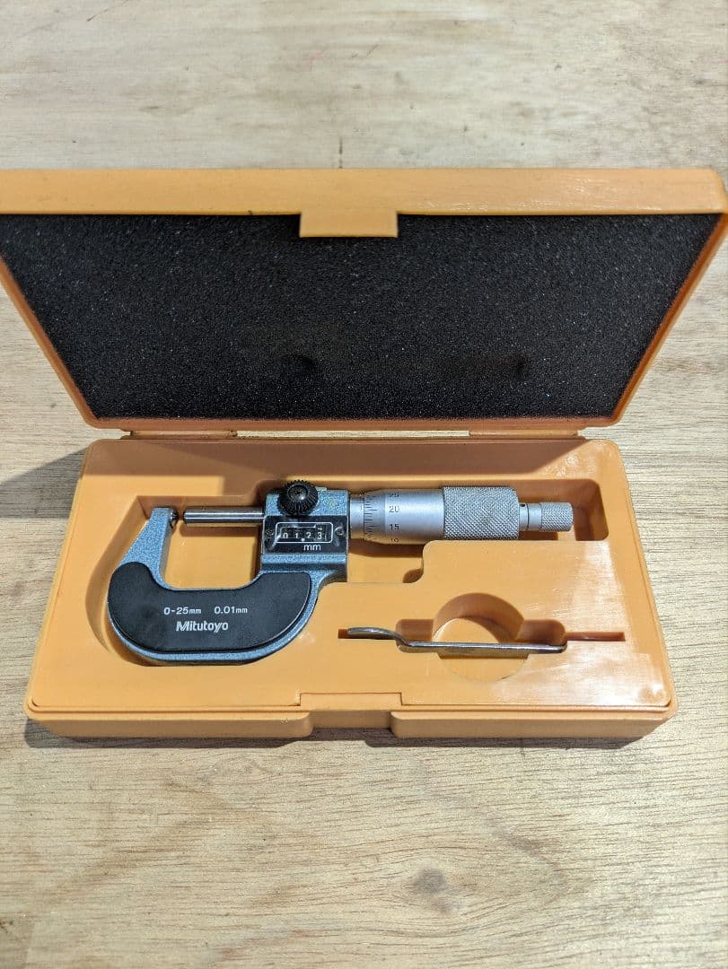 Mitutoyo micrometer (0–25 mm) placed in its orange fitted plastic case on a wooden surface.
