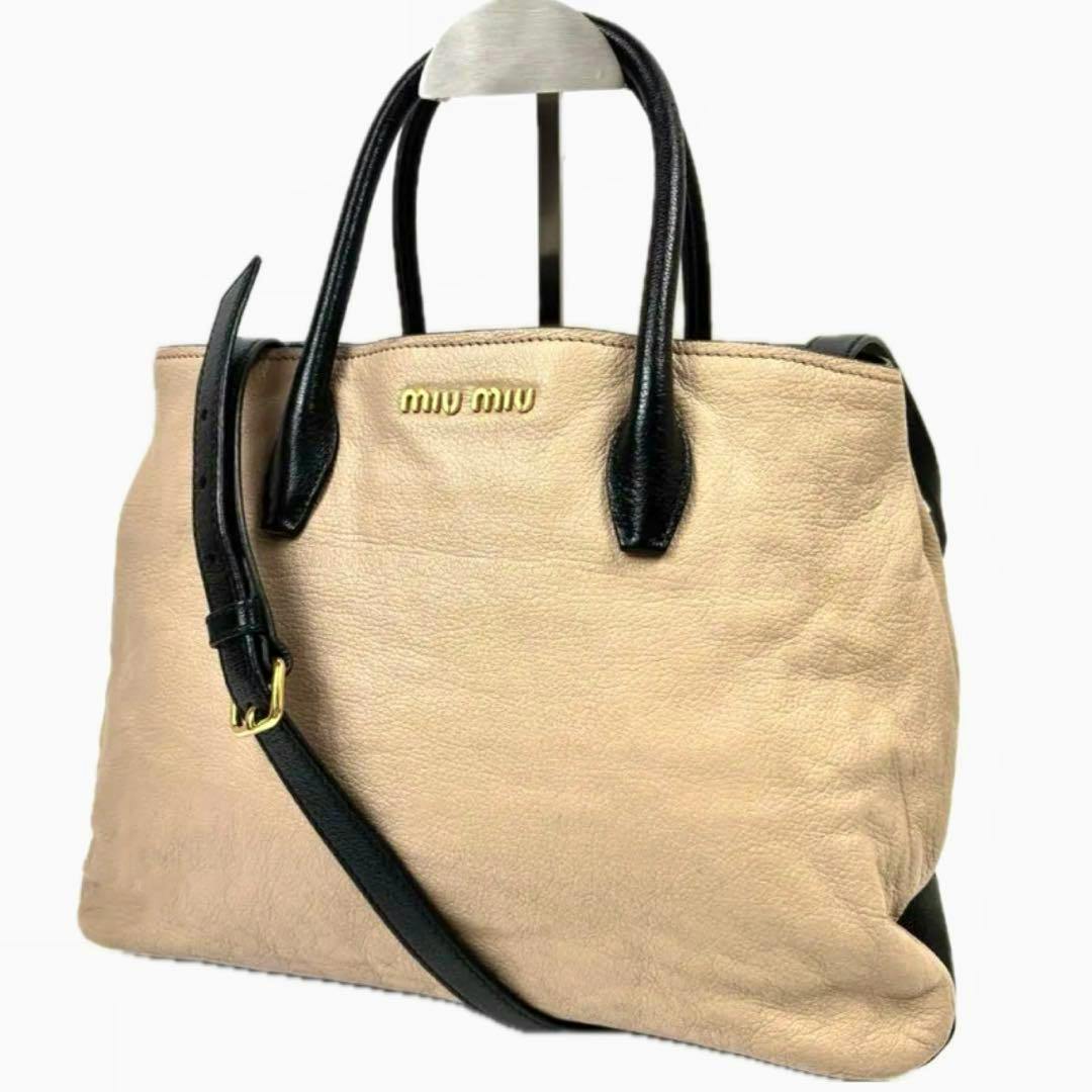 Beige and black miu miu bicolour 2-way leather handbag with top handles and an adjustable black shoulder strap shown from the front.