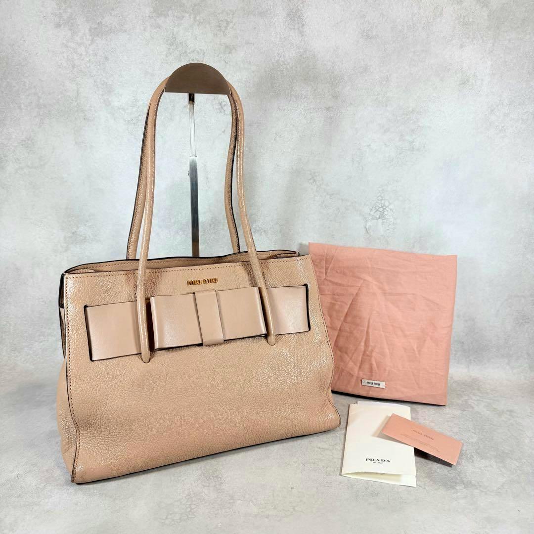 Beige Miu Miu cow leather Madras Fiocco tote bag with front bow, shown on a stand with dust bag and paperwork.