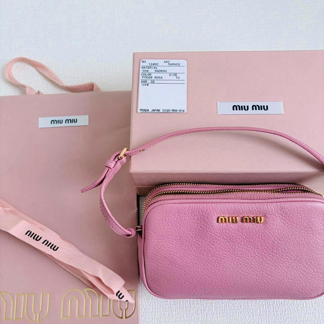 Pink miu miu small pouch/mini bag with strap shown alongside its box, ribbon, and shopping bag.