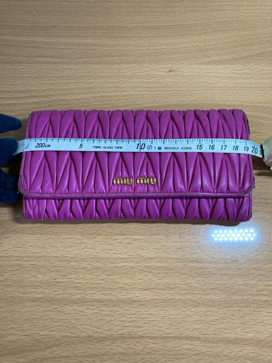 Pink Miu Miu matelassé long wallet on a wooden surface with a measuring tape across it.