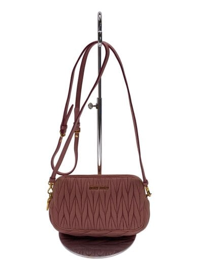Front view of a pink MIU MIU cow leather shoulder bag with a textured quilted front and adjustable strap hanging on a stand.