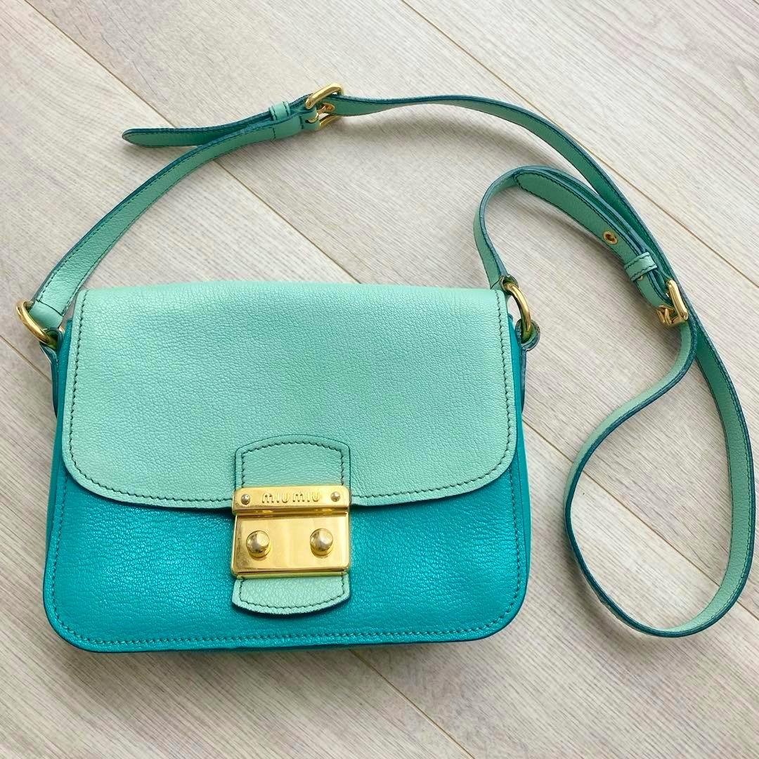 A two-tone mint and teal miumiu leather shoulder bag with a gold clasp and adjustable strap on a light wood floor.