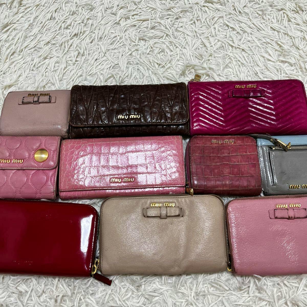 Several miu miu wallets in different colors and styles arranged on a white shag rug.
