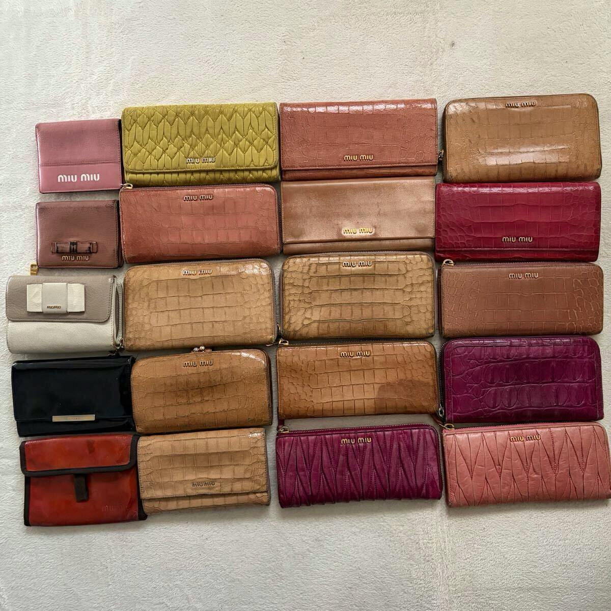 Multiple miumiu leather wallets and long wallets in various colors arranged flat on a light fabric surface.
