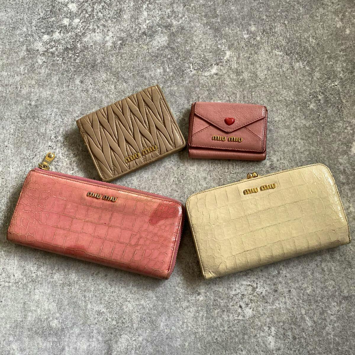Four Miu Miu wallets and a small card wallet in different colors and textures arranged flat on a gray surface.