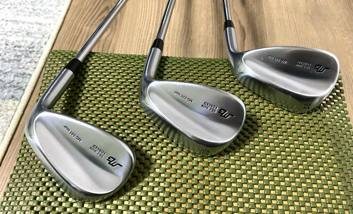 Three Miura MG-S01 wedge heads (50°, 52°, 58°) laid on a green mat showing the club heads and shafts.