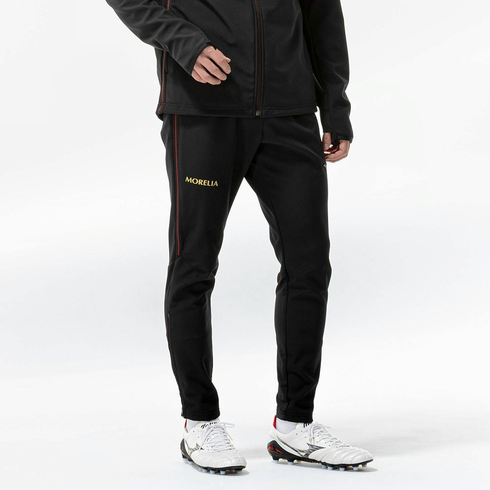 Front view of the black men's pants being worn by a model, showing tapered legs and a "MORELIA" logo on the left thigh.