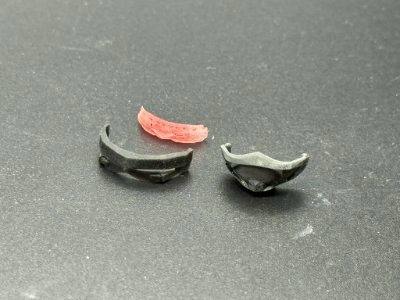 Three small plastic figure parts (two visors and one mask) shown on a gray surface.