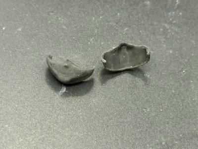 Two small black plastic mask parts for a figure placed on a dark surface.