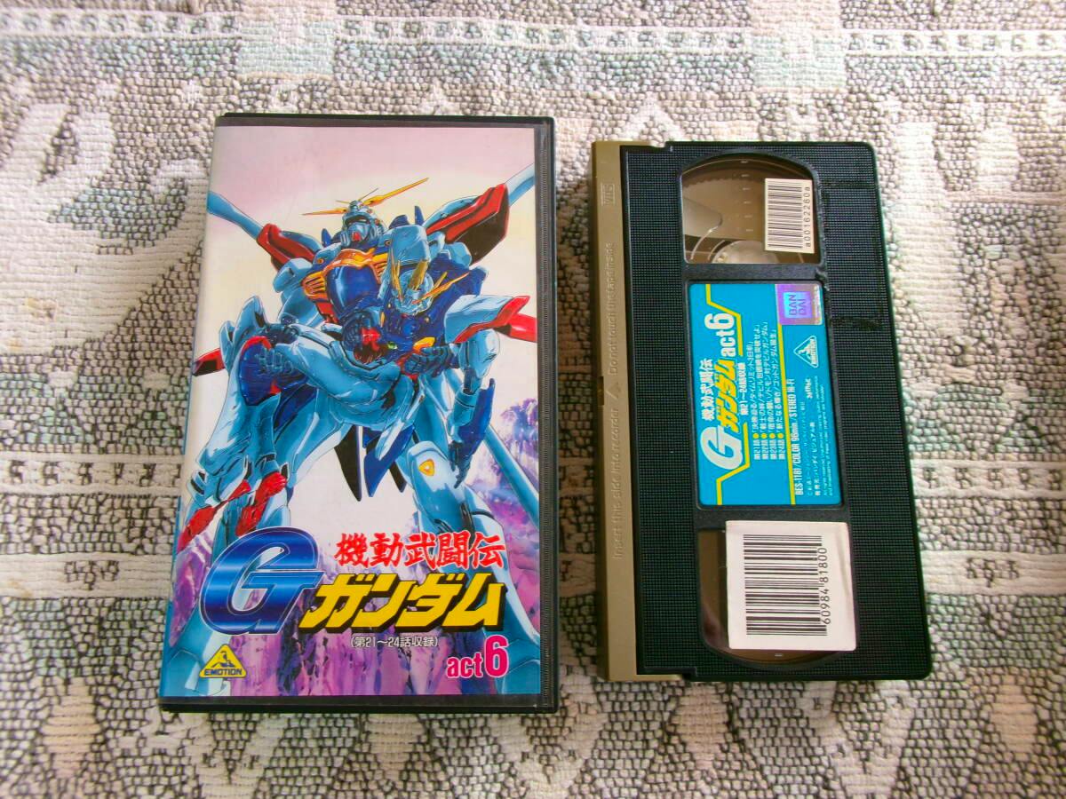 A VHS tape and its case for 機動武闘伝 Ｇガンダム act.6 shown side by side on a patterned surface.