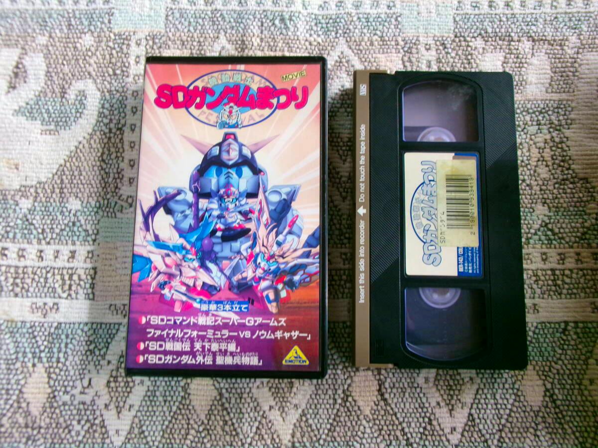 Front cover and VHS tape of the SD Gundam Matsuri (1993 Japanese anime) shown side-by-side on a patterned surface.
