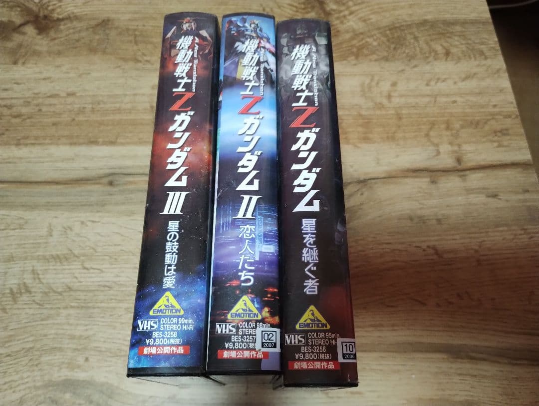 Three VHS tape boxes for 機動戦士Zガンダム 劇場版 (Zeta Gundam) shown by their spines standing side by side on a wooden table.