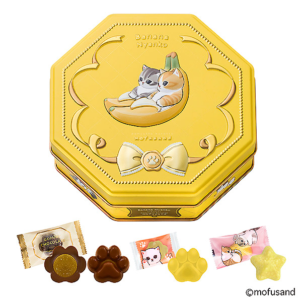 Yellow octagonal tin with a banana-and-cat illustration, with several individually wrapped chocolates and shaped candies displayed in front.