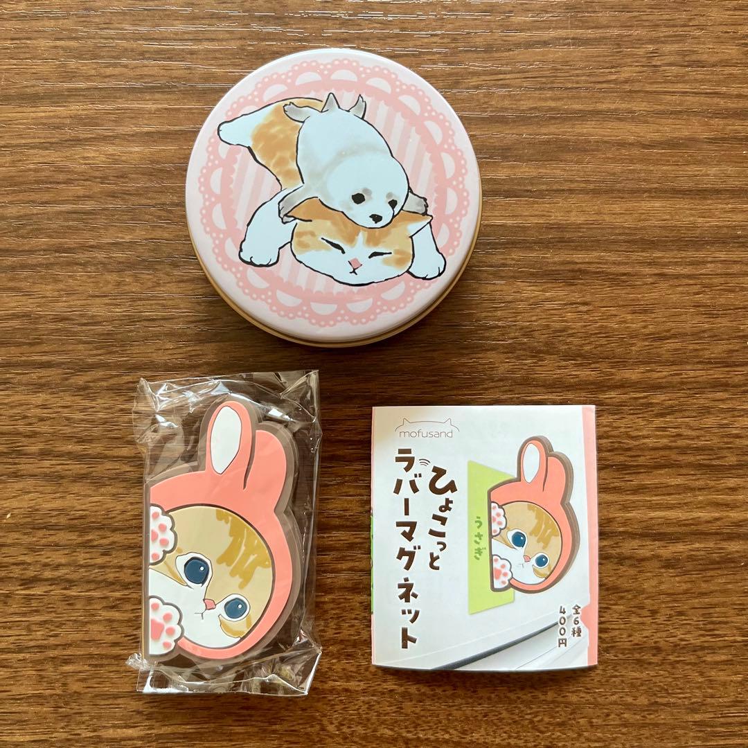A rabbit-shaped packaged rubber fridge magnet and its small illustrated product box displayed below a round tin with a cat illustration on a wooden surface.