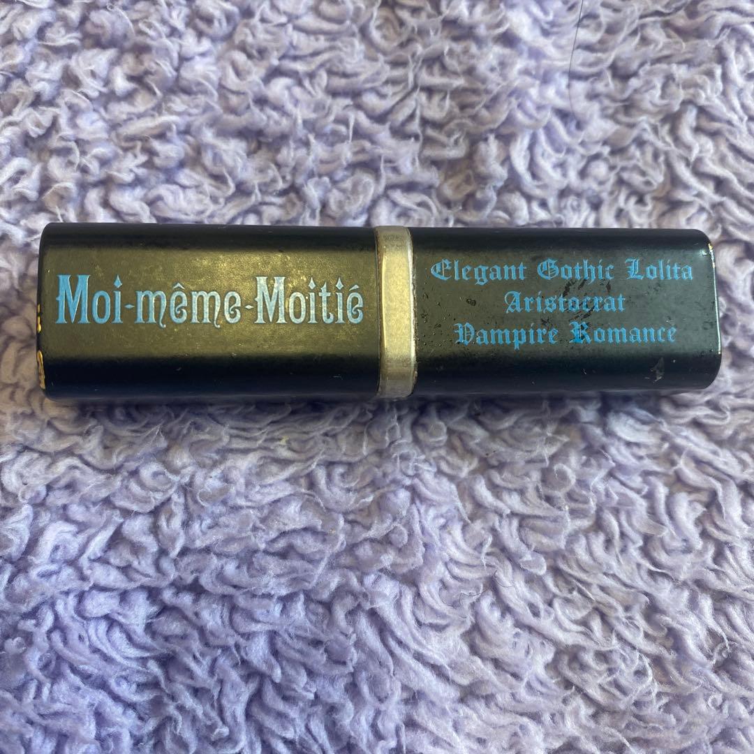 Closed Moi-meme-Moitie lipstick tube showing brand text on a purple textured surface.