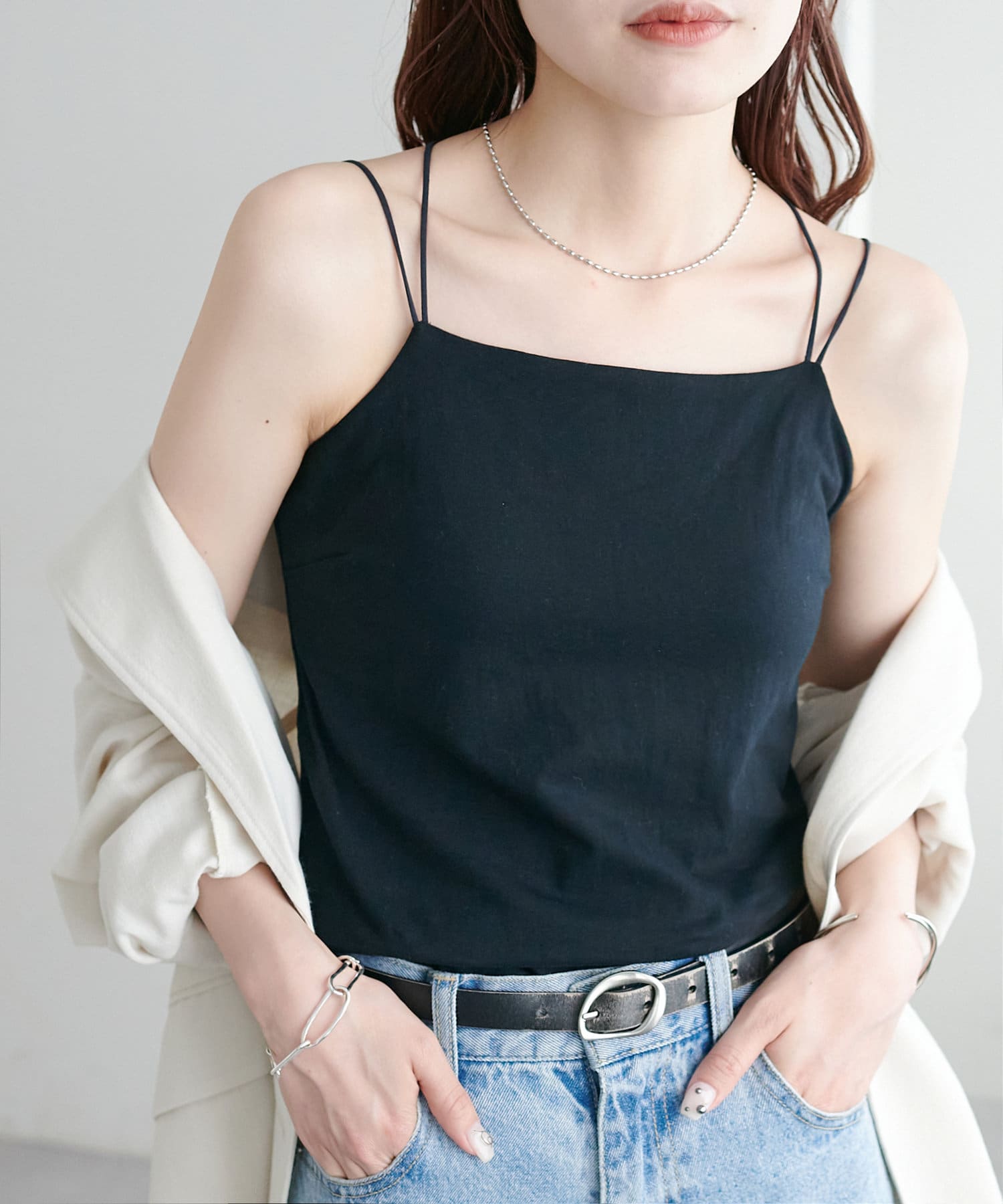 Model wearing a black cup-equipped camisole with thin double shoulder straps, tucked into jeans and layered with a light jacket.