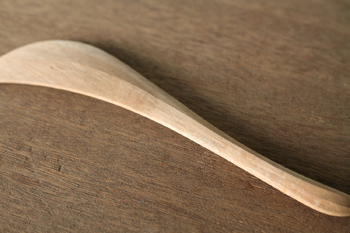 Wooden spatula (turner) photographed lying on a wooden surface, showing the paddle and handle.