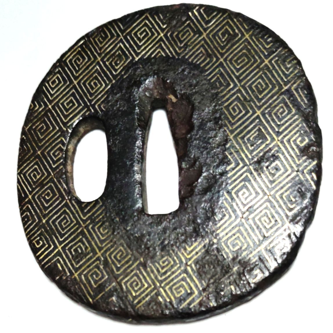 Top-down photo of a round iron tsuba with geometric brass inlay and two openings for sword fittings.