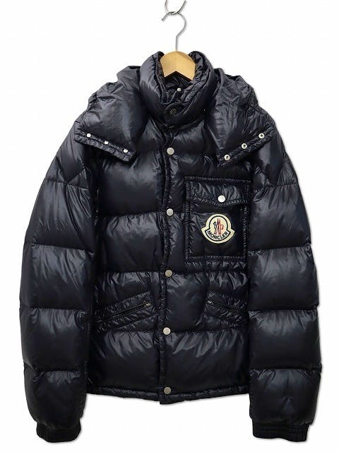 Front view of the navy Moncler nylon men's down jacket with a visible chest logo patch, hung on a hanger.