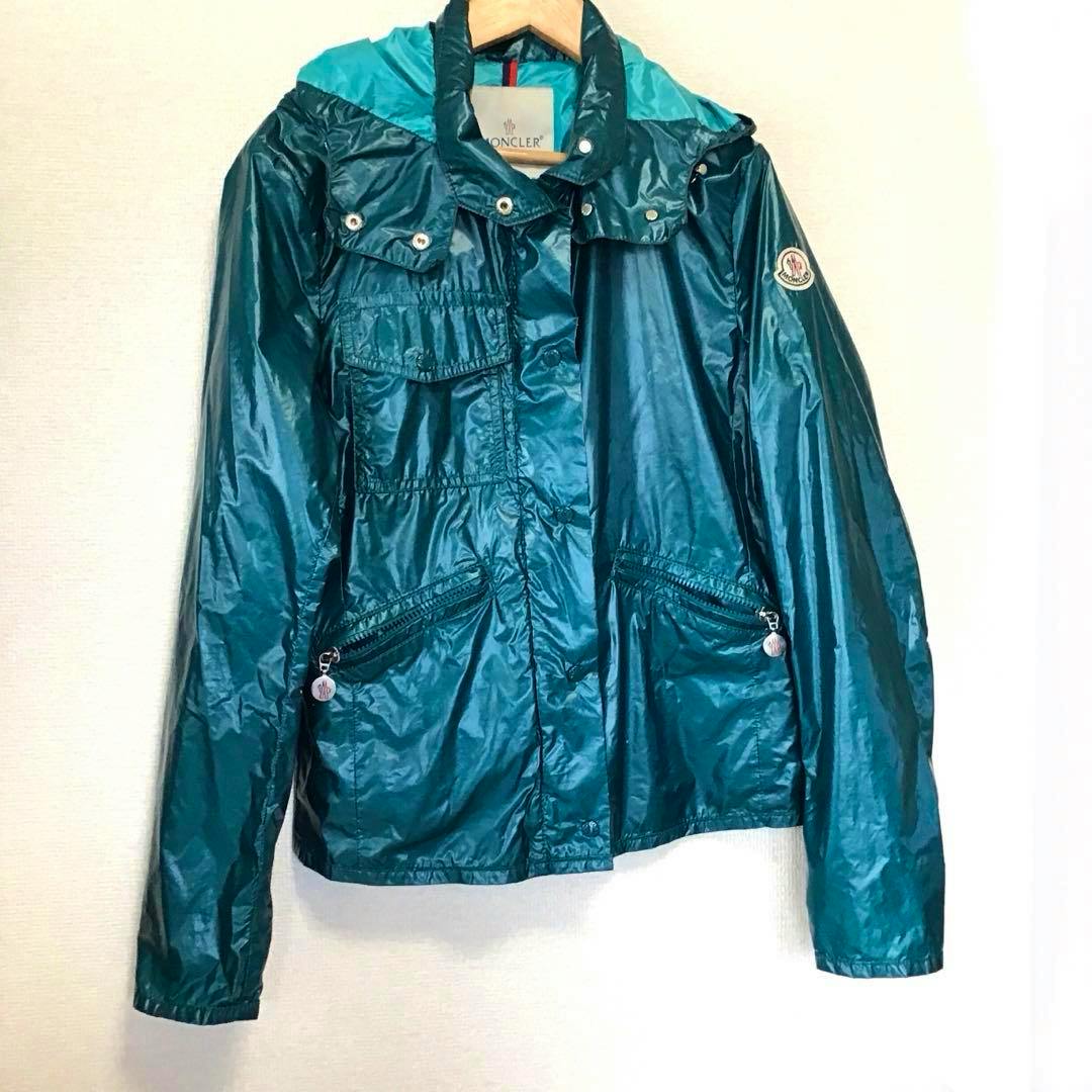 Front view of a Moncler nylon men's windbreaker (size M) in teal hanging on a hanger.