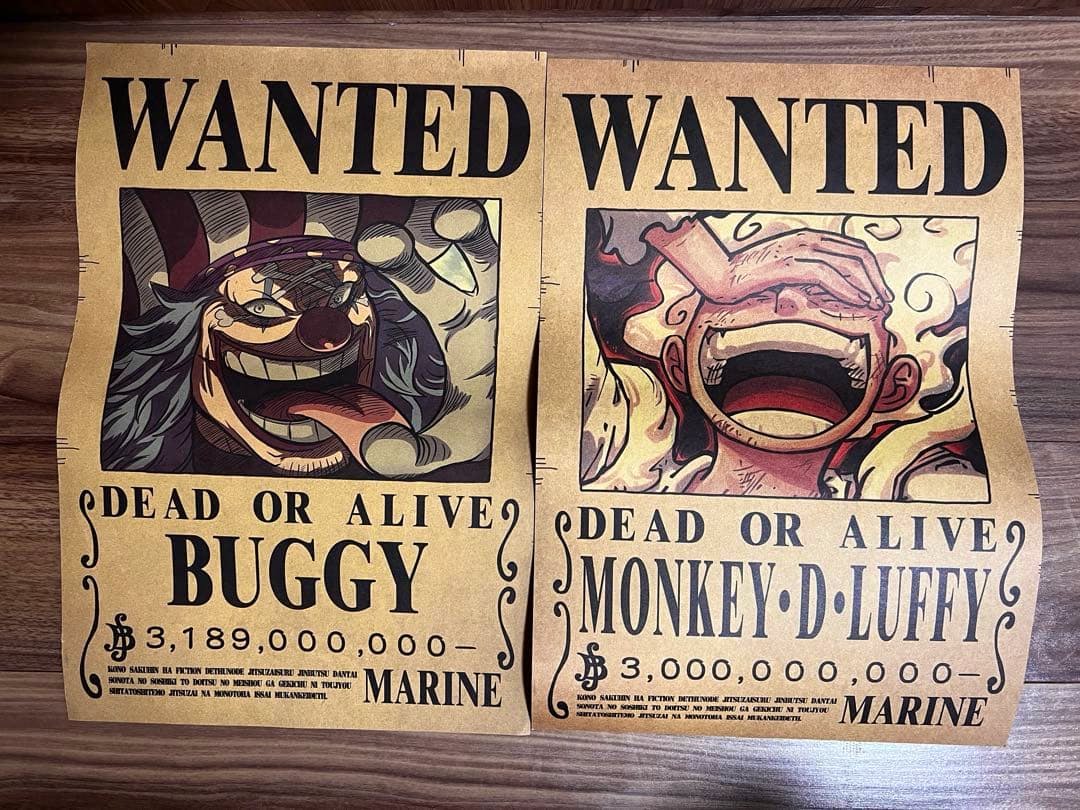 Two wanted-style posters showing Buggy and Monkey D. Luffy laid side-by-side on a wooden floor.