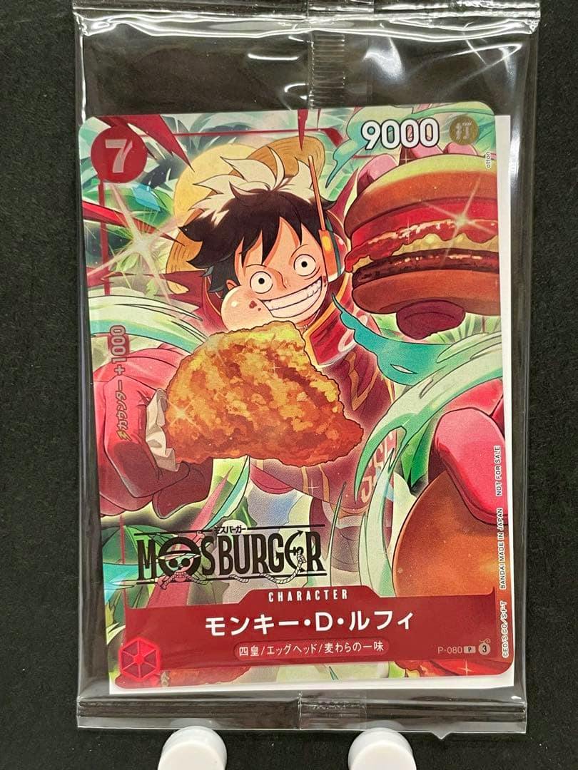 Front of the モンキー・D・ルフィ Mossburger P-080 One Piece trading card in a clear sleeve, showing Luffy holding a piece of fried chicken and a burger.