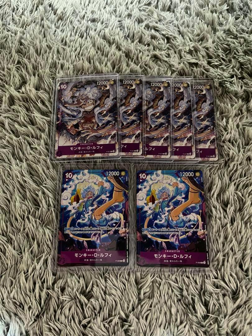 Seven One Piece Monkey D. Luffy trading cards face-up in protective sleeves on a rug.