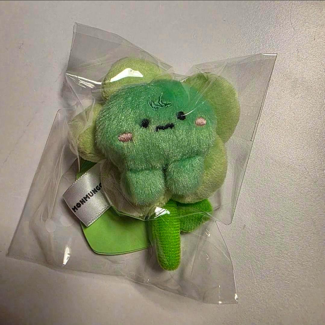 A small green MONMUNGCHI X SWEET BLOSSOM plush (ヒョンウォン) inside clear plastic packaging showing its face and fabric tag.