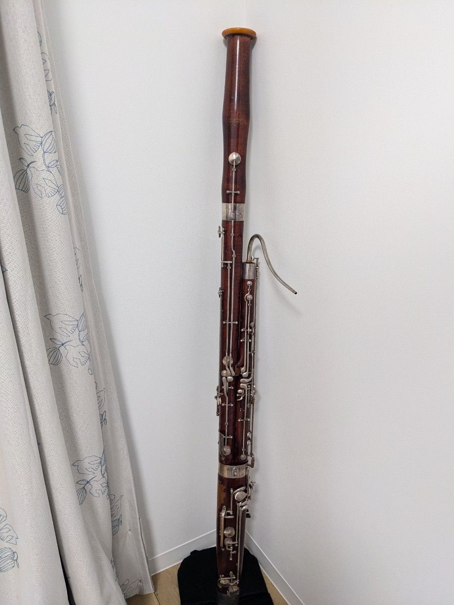 Full MONNIG bassoon (fagott) standing upright against a white wall on a dark cloth.