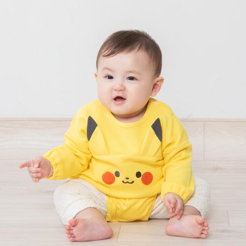 Infant wearing the yellow Pikachu long-sleeve romper with cream leggings, seated on a light floor.