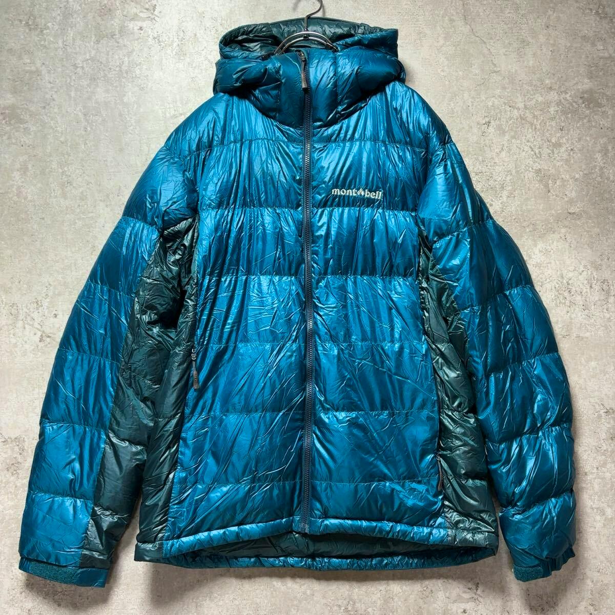 Front view of a blue mont-bell Alpine down parka jacket with hood and zipper hung on a hanger.