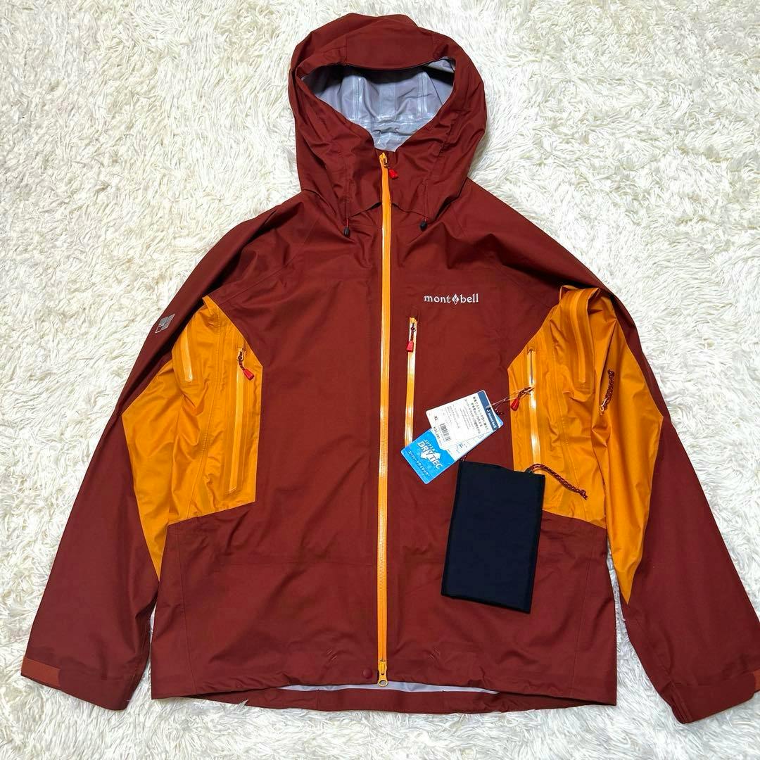 A red Montbell men's hooded jacket with orange inner panels and attached tags laid flat on a white rug.