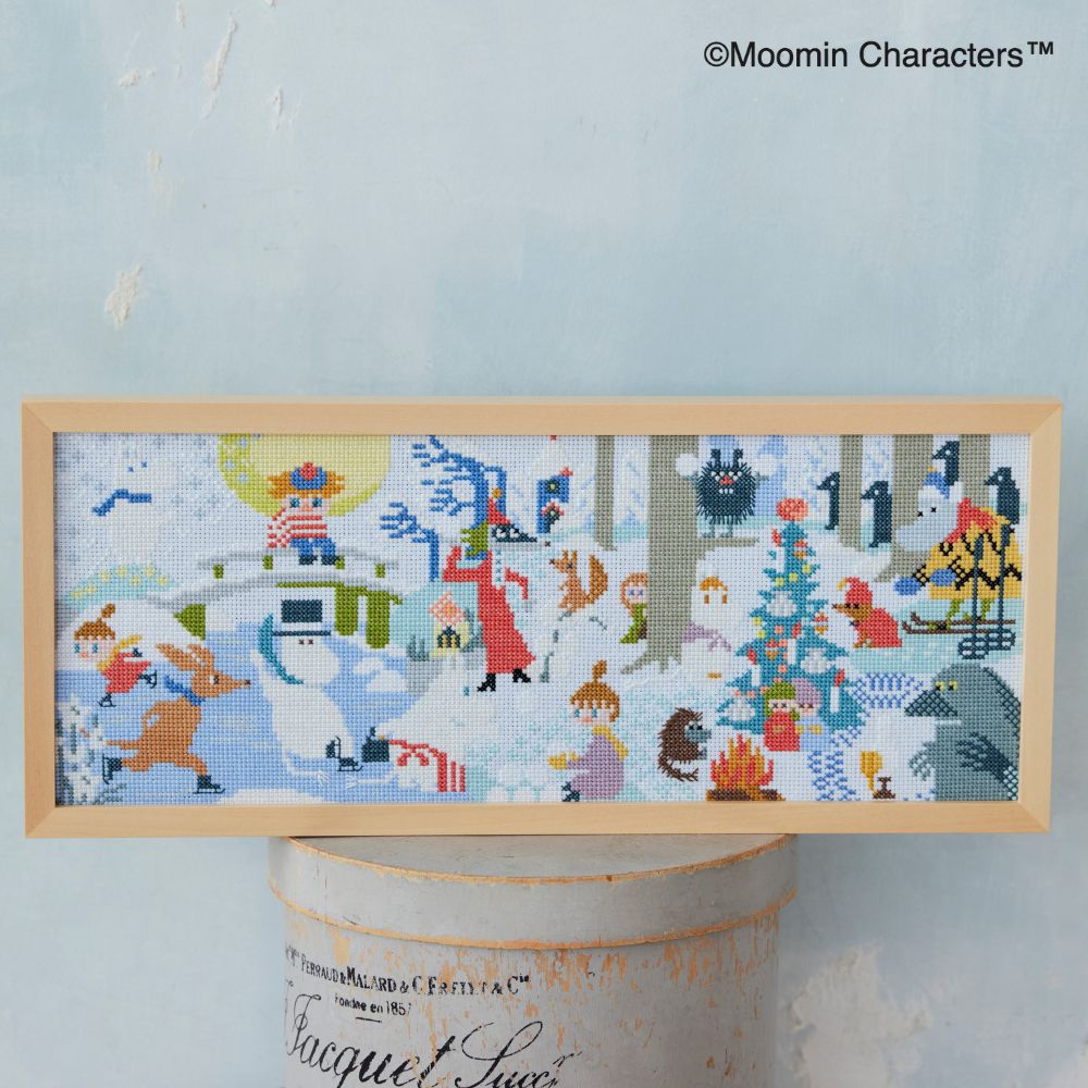 Framed Moomin cross-stitch embroidery showing a winter scene with Moomin characters in a snowy landscape.