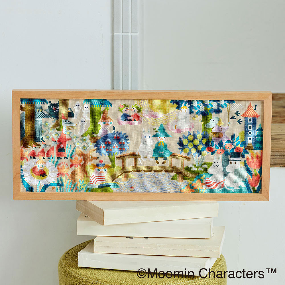 Framed Moomin cross-stitch showing Moomin characters on a bridge in Moomin Valley.