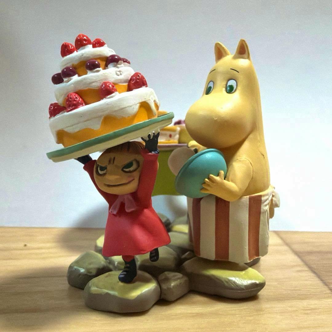 Assembled plastic Moomin figures showing Little My holding a large layered cake and Moominmamma holding a bowl on a rocky base.