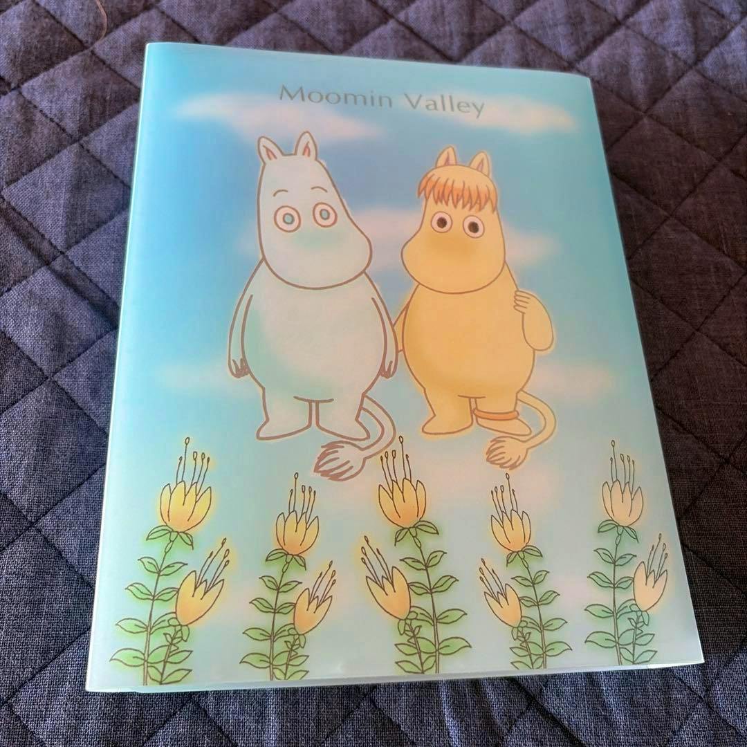 Front of a Moomin Valley acrylic panel showing two Moomin characters and yellow flowers on a light blue background.