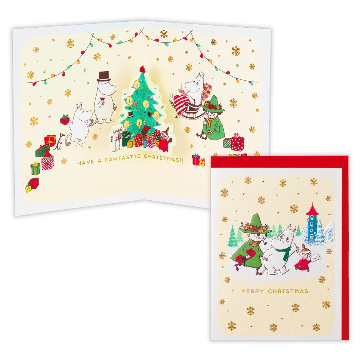 A Moomin Christmas pop-up greeting card showing the front cover with characters and gold snowflakes and the open interior with a 3D Christmas tree and Moomin characters.
