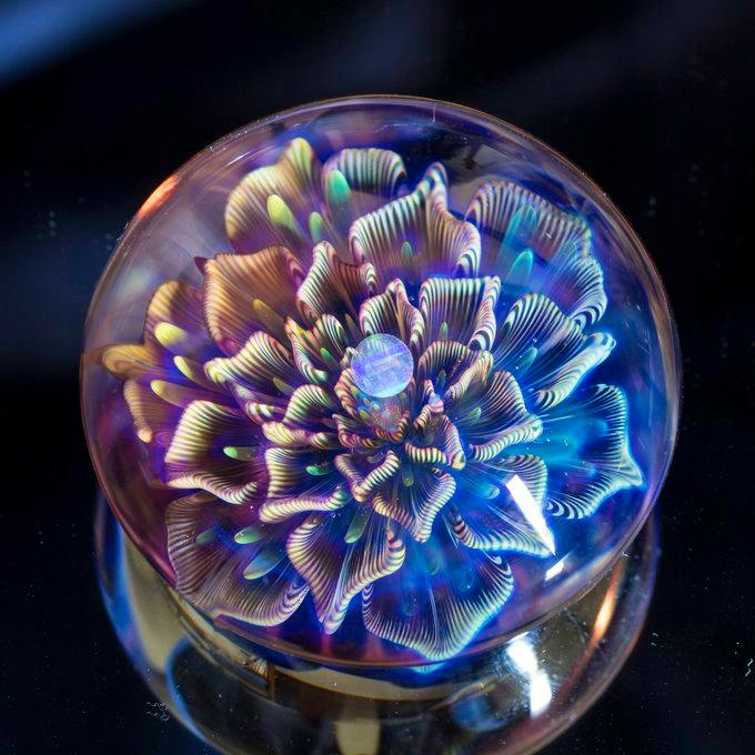 Top-down view of a borosilicate glass paperweight showing an iridescent flower-like design inside.