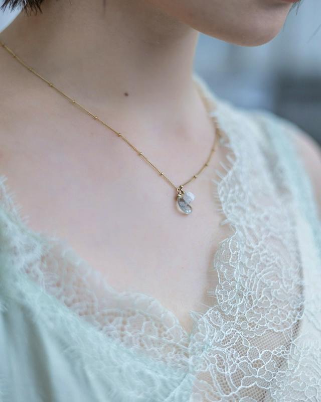 Model wearing the necklace 「月夜の願い」 (14kgf) showing the pendant on a gold chain over a lace top.