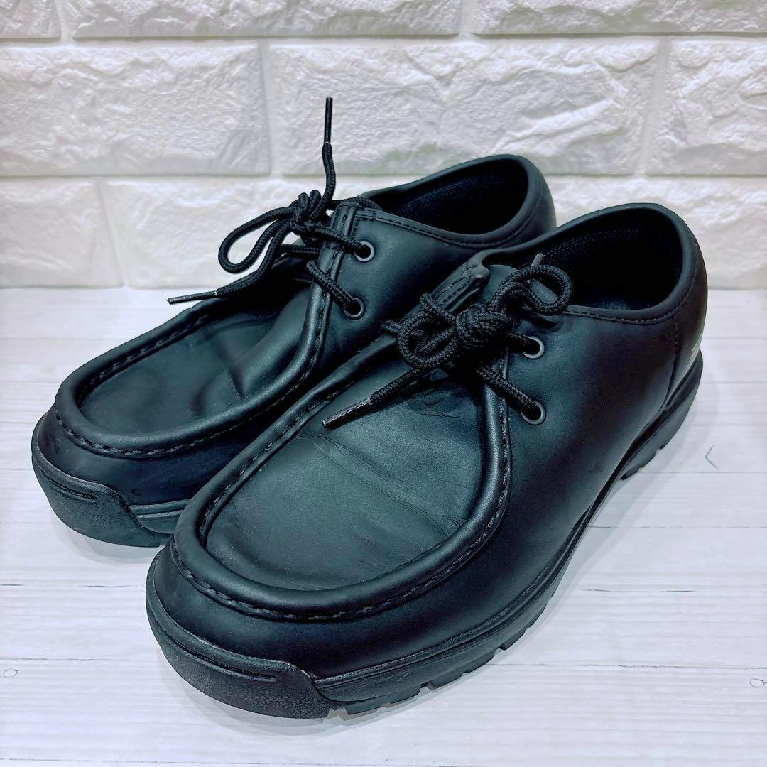 Black MOONSTAR 810s COMUT leather Tyrolean shoes shown at an angle on a light wooden surface with a white brick background.