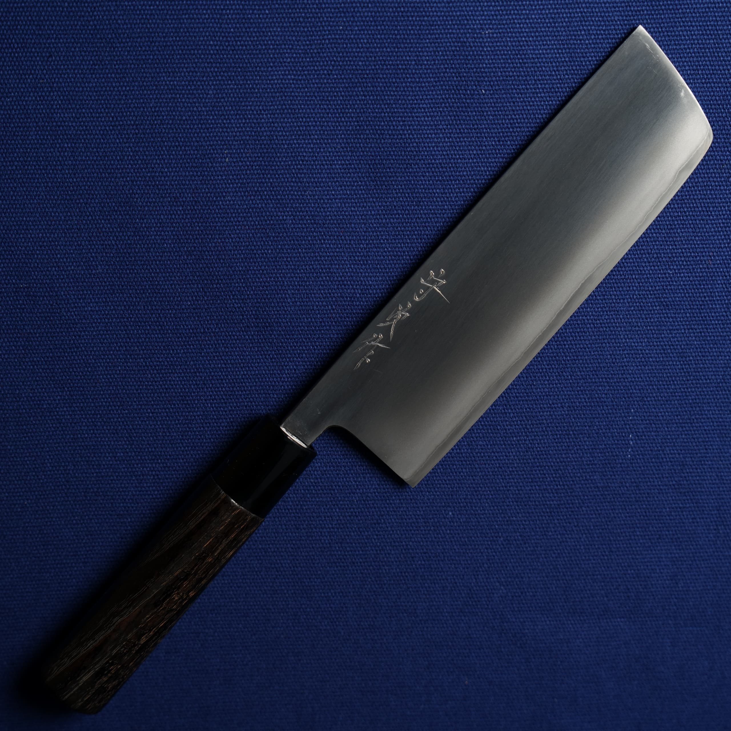 A nakiri-style chef knife with a polished stainless blade and a dark wooden handle shown on a blue background.